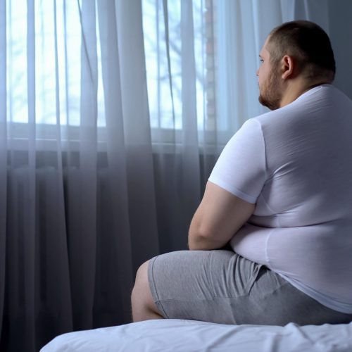 Sad heavy man sitting on bed at home, health problem, depression, insecurities